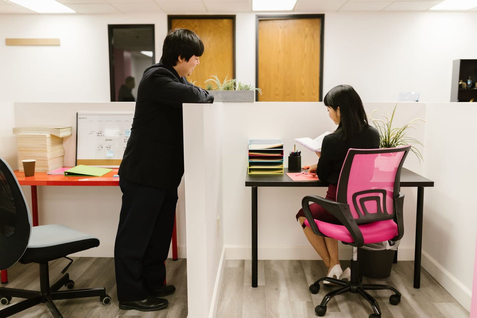 Deux jeunes salariés dans un bureau : un homme debout en costume et une femme assise prenant des notes